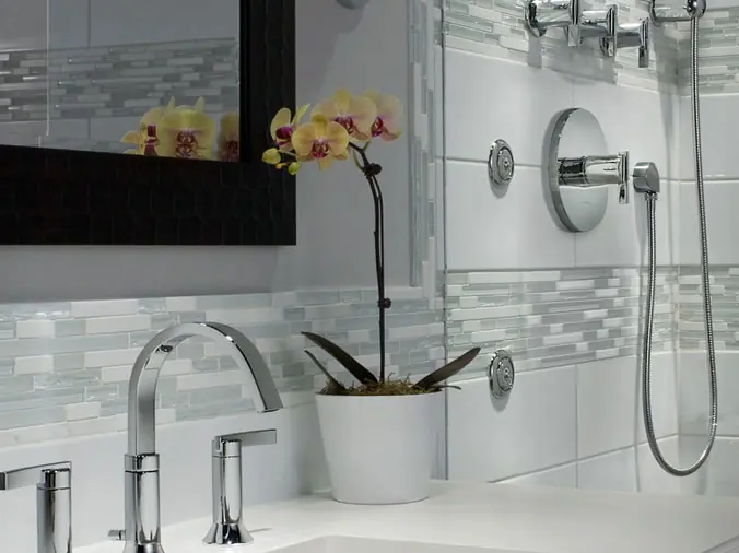 white bathroom with bathroom sink in foreground and shower with chrome fittings in the background